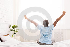 Young man waking up in bed and stretching his arms