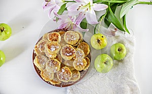 Good morning, breakfast with cheese cakes, green apples and pink lilies on a white table lit by the sun, top view, horizontal