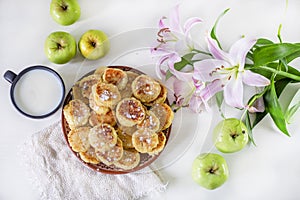 Good morning, breakfast with cheesecakes, green apples, milk and pink lilies on a white table lit by the sun, horizontal