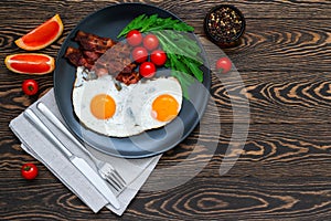 Good morning breakfast with fried eggs, crispy bacon, cherry tomatoes, rocket salad and grapefruit slices served on the wooden tab
