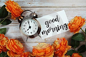 Good Morning card and alarm clock with orange flower decoration on wooden background