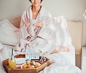 Good morning concept. Croped woman in bathrobe sitting on the bed, drinking coffee and has her breakfast in bed with Have a nice