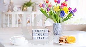 Good morning concept. Romantic breakfast - fresh flowers, cup of hot drink, cookies, orange, lightbox with message Enjoy