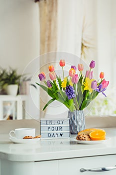 Good morning concept. Romantic breakfast - fresh flowers, cup of hot drink, cookies, orange, lightbox with message Enjoy