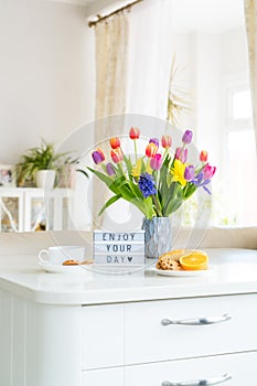 Good morning concept. Romantic breakfast - fresh flowers, cup of hot drink, cookies, orange, lightbox with message Enjoy your day