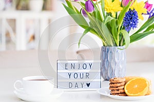 Good morning concept. Romantic breakfast - fresh flowers in vase, cup of hot drink, cookies, orange, lightbox with