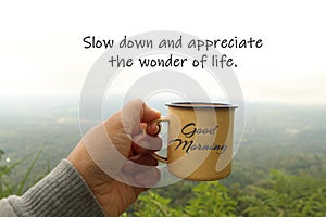 Good Morning greeting on cup of coffee in hand with grateful inspirational quote - Slow down and appreciate the wonder of life.