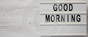 `Good morning` on a lightbox on a white wooden background, top view. Flat lay, overhead, from above. Copy space