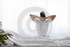 Good Morning. Man With Hands Behind Head Sitting On Bed, Rear View