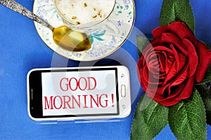 Good morning-a message on the smartphone screen, a Cup of delicious coffee for cheerfulness, a red rose decoration for a joyful