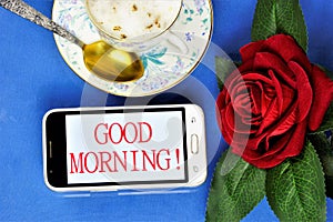 Good morning-a message on the smartphone screen, a Cup of delicious coffee for cheerfulness, a red rose decoration for a joyful photo
