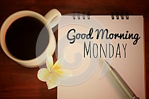 Good morning Monday. Happy Monday concept. With a cup of morning coffee, text message on notebook, pen and a flower.