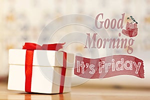 Good morning it`s friday message with white gift box with red ribbon on wood background