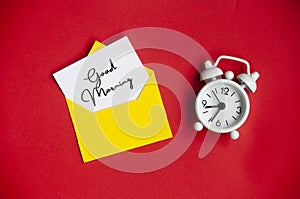 Good morning text on white notepad with envelope and alarm clock background.