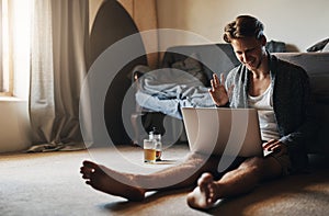 Good morning to you too. a young man making a video call on his laptop while sitting on the floor at home.