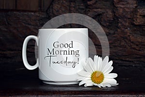 Good morning Tuesday. A Tuesday coffee concept with a white cup of coffee or tea and a daisy flower decoration on the table