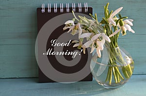 Good Morning.White snowdrop spring flowers in a glass vase on a light blue wooden background