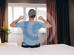 Good morning Young man waking up in bed and stretching his arms, back view, copy space.