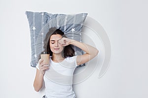 Good morning. Young woman drinking coffee with a pillow under her head,