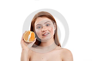 Good for my skin. Portrait of cute red-haired girl with freckles on face holding a piece of orange and smiling at camera