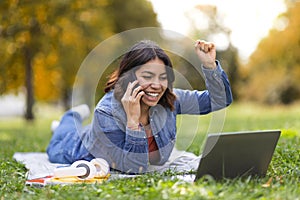 Good News. Joyful Arab Woman Talking On Cellphone And Using Laptop Outdoors
