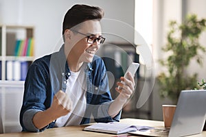 Good News. Joyful Man Celebrating Success With Smartphone At Workplace In Office