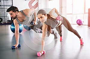 Good picture of boy and girl standing on the carpet with the dumbells in one hand and putting another hand with a