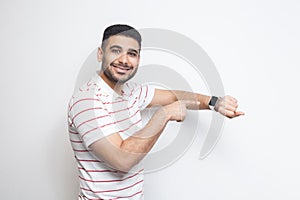 Good result and ontime. Happy handsome bearded young man in striped t-shirt standing, showing his smart watch and looking at