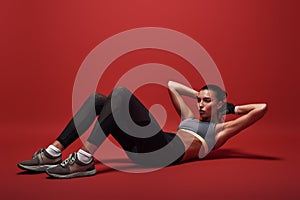 In a good shape. Sportswoman lying over red background, working her abs