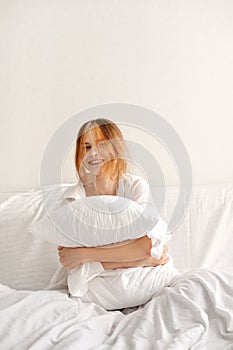 Good sleeping, time to sleep, youth daily health habit concept. Teenager girl sitting on bed, embracing pillow and smiling. White