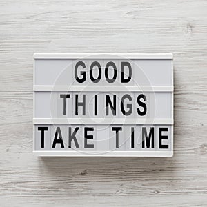 `Good things take time` words on a lightbox on a white wooden background, top view. Overhead, from above, flat lay. Close-up