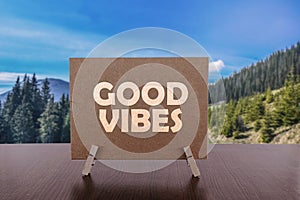 Good vibes text on card on the table with sunny summer mountains background