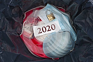 Goodbye 2020 concept: The inside of a trashbin with surgical masks, sanitizing gel, a padlock and a slip of paper with the