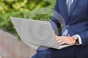 Goodly young man working on laptop while sitting outdoors . Business concept.