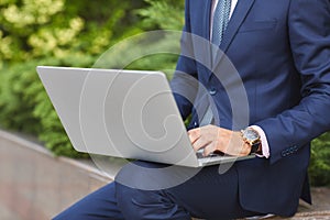 Goodly young man working on laptop while sitting outdoors . Business concept.