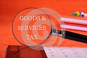 Goods and services and tax text written through a magnifying glass on an orange background