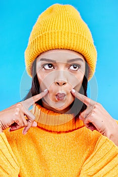 Goofy woman in winter fashion with comic expression, beanie and fun isolated on blue background. Style, happiness and