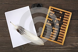 A goose feather lies on a pile of white sheets of paper. Old accounts and a retro inkwell are located side by side on a wooden tab