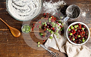 Gooseberries and red currants on a wooden table, a bowl of flour, a wooden spoon and a linen towel. Top view
