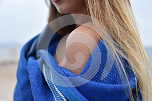 Goosebumps from the cold on the shoulder of girl or woman wrapped in a blue blanket on the beach. shallow depth of field