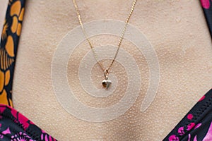 Goosebumps on a woman`s skin. Gold pendant in the shape of a heart.