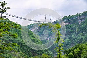 A gorge in the mountains with a suspension bridge over it. Skybridge suspension bridge over a precipice on a cloudy day. SkyPark,