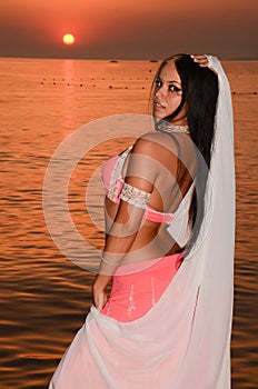 Gorgeos girl with veil posing on the beach in front of the sunset