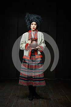 Gorgeouns young woman in ukrainian traditional costume holding clay jug of milk