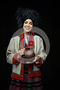 Gorgeouns young woman in ukrainian traditional costume holding clay jug of milk