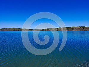 A gorgeous aerial shot of a vast blue lake with lush green and autumn colored trees reflecting off the lake at Lake Horton Park