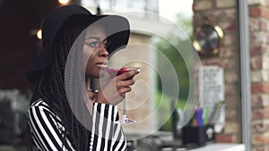 Gorgeous african american business lady in black hat drinking cocktail at bar and enjoying her drink