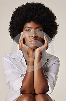 Gorgeous african american woman with beautiful afro wearing a white shirt and sitting with her hands around her face