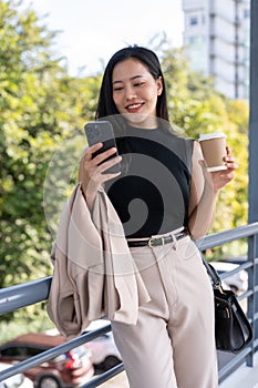 A gorgeous Asian businesswoman is responding to messages on her phone on a skywalk