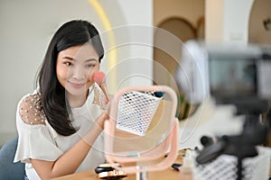 Gorgeous Asian female freelance beauty blogger applying brush-on on her cheekbone